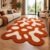 Abstract blob tufted rug with ivory shapes on rust orange beside a cream sofa