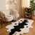 Black and white abstract cow print tufted rug on a wood floor beside a cream bouclé loveseat